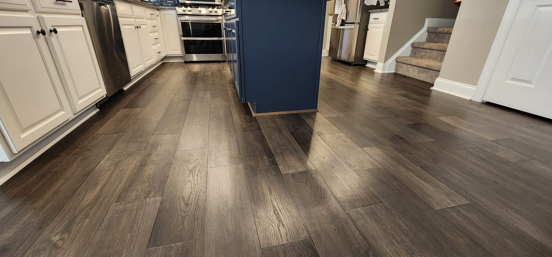 Wide-plank hardwood floors installed in a kitchen with a navy island by Frankie D’s Flooring
