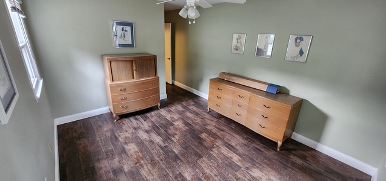 Dark plank flooring under vintage oak dressers in a sage bedroom by Frankie D’s Flooring